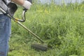 A man mows the thick tall grass with a gasoline trimmer. The lawn mower`s work