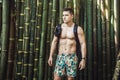 Man with muscle body wearing swimming shorts and backpack at tropical bamboo background