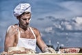 Man muscular baker or cook kneading dough in bowl. Bakery concept. Baker at working surface covered with flour, kneading