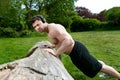 Muscular man, wearing headphones training with pressups against a fallen tree in park Royalty Free Stock Photo