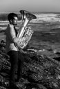 A man musician play a tuba on the seashore. Black and white photo.