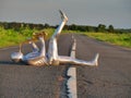 Man musician saxophonist in full body-hugging silver and silver electric suit holding golden alto saxophone, lies on empty road in