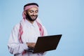 Man in muslim thobe texting on laptop