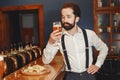 Man with a mustache and beard stands at the bar and drinks alcohol from a glass. Royalty Free Stock Photo