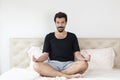 Man with mustache meditating while sitting on bed in morning. Young man doing yoga in bed. Male meditating on bed at home.