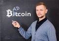 Man near a black school board on which is written bitkoin, part of the word Bitcoin is replaced by Bad