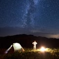 Man near tent and bonfire is meeting Milky Way at the starry sky against background of mountains. Royalty Free Stock Photo