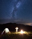 Man near tent and bonfire is meeting Milky Way at the starry sky against background of mountains. Royalty Free Stock Photo