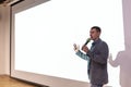 A man near the white screen of the projector with a micraphone talks about the project. Royalty Free Stock Photo