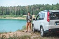 man near white suv car at the edge looking at lake with blue water