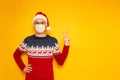 man in New Year& x27;s sweater with reindeer, medical mask on his face, Santa Claus hat shows sign of V, peace, victory Royalty Free Stock Photo