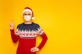 man in New Year's sweater with reindeer, medical mask on his face, Santa Claus hat shows sign of V, peace, victory Royalty Free Stock Photo