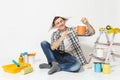 Man in newspaper hat sitting on floor with paint brush, can, instruments for renovation apartment room isolated on white Royalty Free Stock Photo