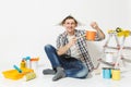 Man in newspaper hat sitting on floor with paint brush, can, instruments for renovation apartment room isolated on white Royalty Free Stock Photo