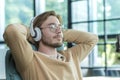 A man in an office on a chair with his arms folded is listening to music in headphones