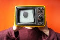 Man with old retro tv head with damaged screen on bright orange background, studio. Multimedia, brainwashing, social concept.