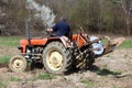 Man on older tractor preparing to plow the field surrounded with uncut grass and dense trees in background