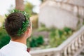 A man in an olive wreath in a white shirt against the background of an old staircase, back view, close-up