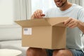 Happy man opening parcel on sofa at home, closeup. Internet shopping