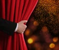 Man opening red front curtain against blurred lights. Bokeh effect Royalty Free Stock Photo