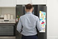 Man opening refrigerator door with child`s drawings, notes and magnets Royalty Free Stock Photo