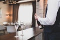 Man opens a bottle of sparkling wine. Two glasses stand on bar counter. The action takes place inside the cozy hotel room Royalty Free Stock Photo