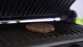 Man opens lid of grill with frying patty in light kitchen