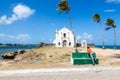 A man in an orange t-shirt is looking at the Church fortress of San Antonio on Mozambique island, with three palm trees on sand. Royalty Free Stock Photo