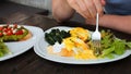 Man ordered poached egg, salad, avocado toast in cafe. Man pierces cucumber with fork dips in yolk on poached egg. Order Royalty Free Stock Photo