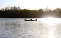 Man out in fishing boat on river in early foggy morning with smoke from outboard motor showing against trees