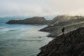 Man in outdoor cloths standing alone on a hill by the ocean overlooking the Point Bonita Lighthouse on a foggy San Francisco day,