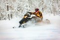 Human in the outfit of a racer in a multi-color jumpsuit and a helmet, driving a snowmobile by the deep snow surface on background