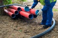 A man in overalls and a bright vest closes large red plastic pipes with blue caps Royalty Free Stock Photo