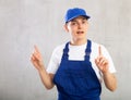 Man in overalls and cap is actively gesticulating-he spread hands to sides,raised index fingers up