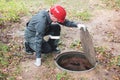 a man in overalls opened a sewer hatch and looks into a septic tank. Cleaning of sewers and drains