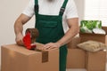 Man packing box with adhesive tape indoors. Moving service