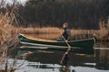 Man paddling a beautiful green canoe on the pond, calm late autumn nature. Active lifestyle, a person enjoying tranquil early