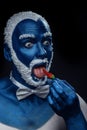 Man painted in blue color with snowy hair and beard eating chili pepper Royalty Free Stock Photo