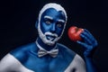 Man painted in blue color with snowy hair and beard holding tomato