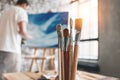 Man painter working in workshop in back of the canvas and drawing. Brushes close up on wooden table in studio. Flare effect Royalty Free Stock Photo