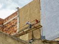 A man painting a big wall from a rustic and poorly secure hanging scaffold