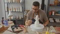 Man painting a ceramic vase on a pottery wheel in studio using a small brush and wearing an apron; creative focus Royalty Free Stock Photo
