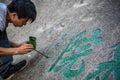 Man painting chinese calligraphy characters on a rock