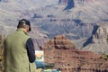 A man watercolor painting the Grand Canyon while he sits on the South Rim overlooking it`s beauty