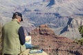 A man watercolor painting the Grand Canyon while he sits on the South Rim overlooking it`s beauty