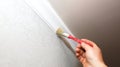 Man is painting gypsum baseboard with brush on ceiling. Maintenance repair works in the flat. Restoration indoors. Drywall panel Royalty Free Stock Photo