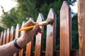 Man painting wood stain at picket fence