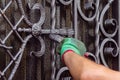 A man paints a gate with forged elements. On his hand is a green glove, near the elbow of a graze.