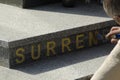 Man paints Surrender word with golden paint on a granite stone slab
