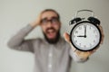 Man in panic holds alarm clock and head in fear of deadline